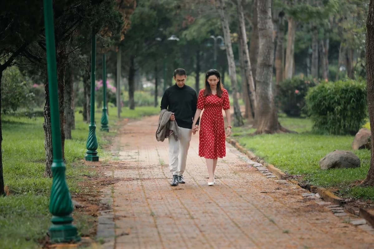 Hai người nắm tay đi bộ trên lối đi trong công viên