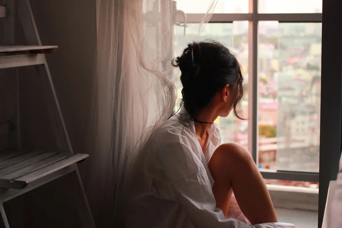 Người phụ nữ ngồi một mình bên cửa sổ nhìn ra thành phố lúc chiều muộn