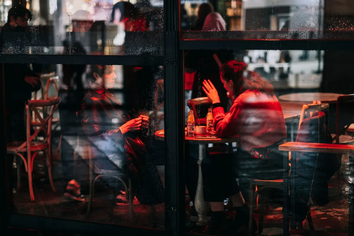 Người ngồi trong quán cà phê kính, ngoài trời đang mưa