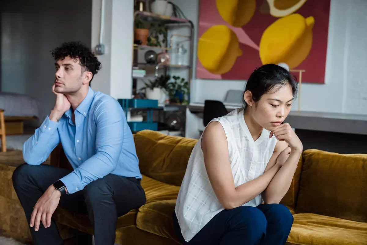 Một cặp đôi ngồi hai đầu ghế sofa, mỗi người nhìn về một hướng