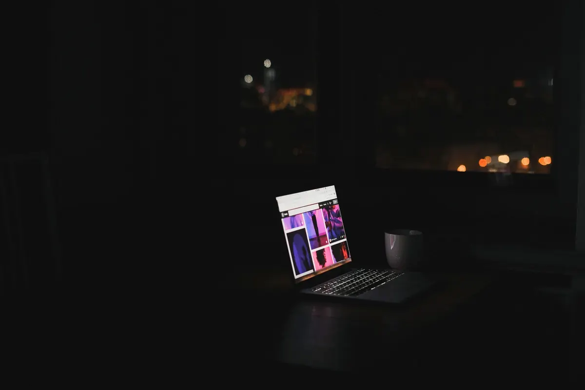 Màn hình laptop sáng trong phòng tối, ngoài cửa sổ là thành phố về đêm