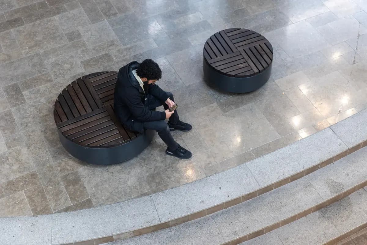 Một người ngồi một mình trên ghế, nhìn màn hình điện thoại