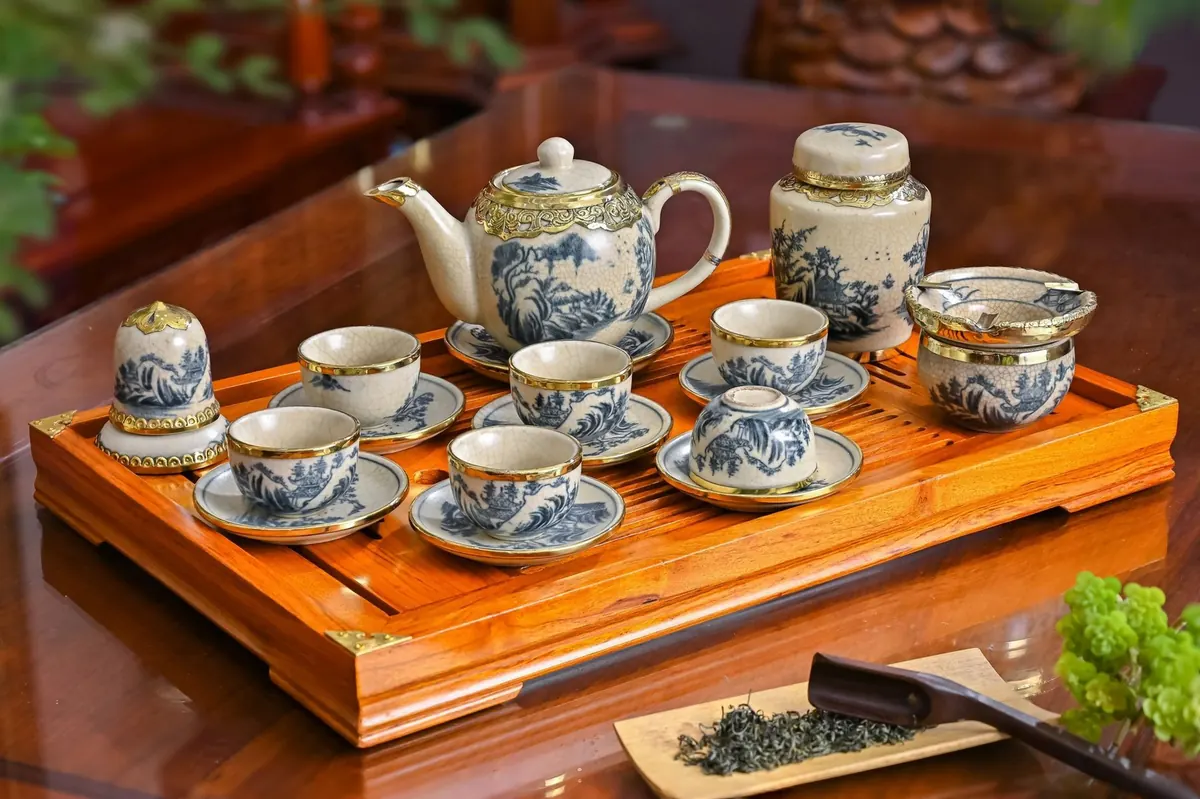Bộ ấm chén men lam trên khay gỗ cạnh một nắm chè khô