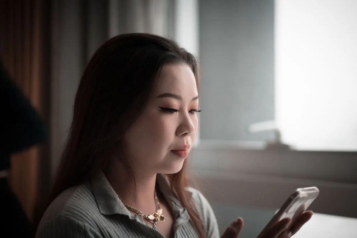 Cô gái châu Á tóc dài cầm điện thoại, nét mặt trầm ngâm trong căn phòng ánh sáng dịu