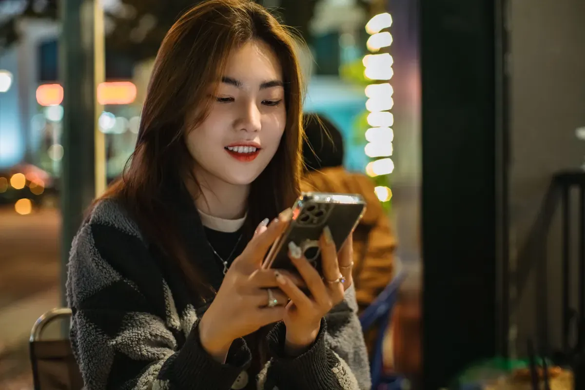 Một người ngồi ngoài trời buổi tối, mỉm cười khi nhắn tin
